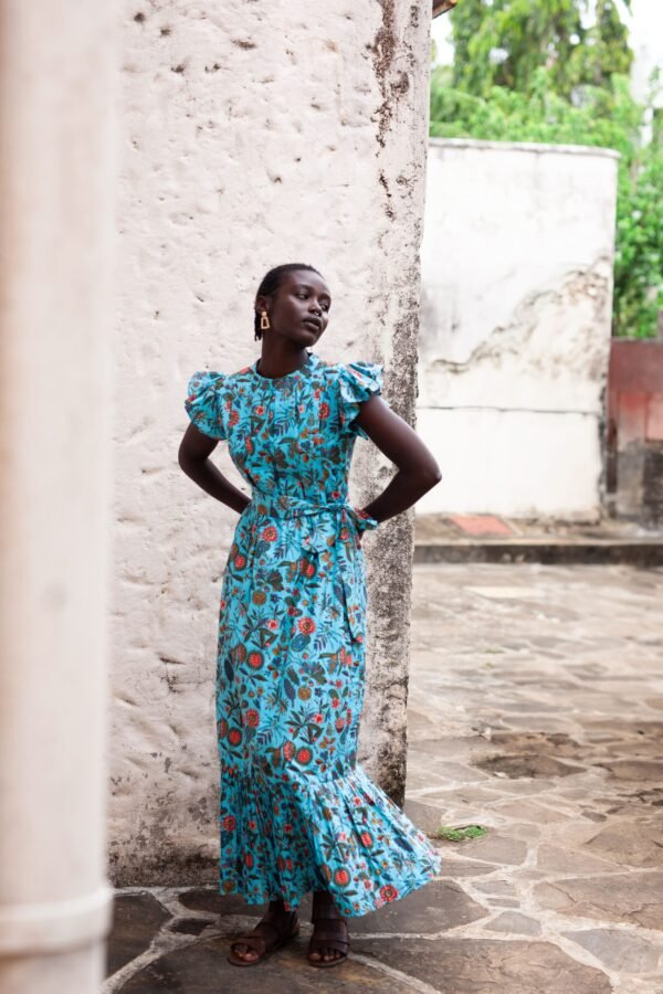 Dress made from hand block printed cotton in soft hues, featuring pleated details, a round neckline, and off-shoulder ruffles. The slim-fitted bodice hugs curves, flowing into a floor-length skirt. Includes a detachable belt and inseam pockets.