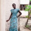 Dress made from hand block printed cotton in soft hues, featuring pleated details, a round neckline, and off-shoulder ruffles. The slim-fitted bodice hugs curves, flowing into a floor-length skirt. Includes a detachable belt and inseam pockets.